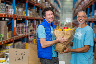 Happy volunteers holding a grocery bag and looking the camera