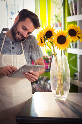 Male florist talking on mobile phone while using digital tablet