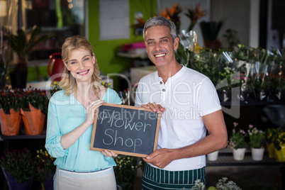 Smiling florists holding flower shop sign on slate in flower sho