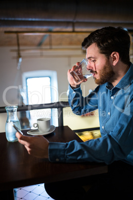 Man having water while text messaging on mobile phone