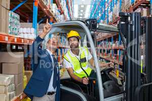 Worker driving forklift discussing with businessman