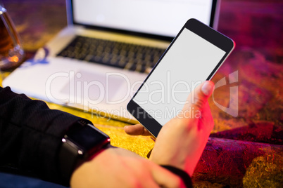 Man using mobile phone with laptop on table at bar counter