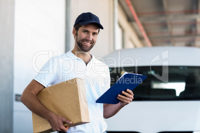 Delivery man is holding a cardboard box and a clipboard and posi