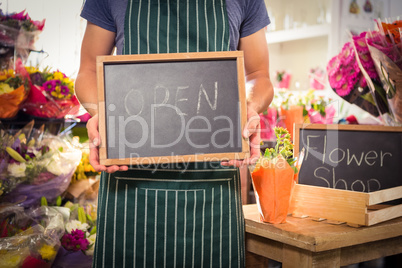 Male florist holding open sign on slate at his flower shop