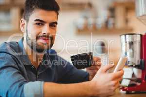 Young man holding mobile phone and coffee cup