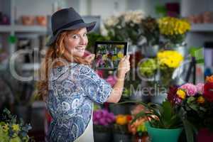 Female florist taking photograph of flowers from digital tablet