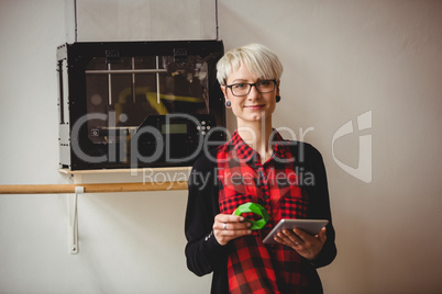 Female graphic designer holding model while using digital tablet