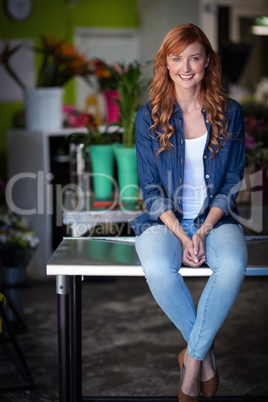 Happy female florist sitting on table in flower shop