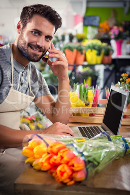 Male florist talking on mobile phone while using laptop