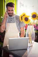 Male florist talking on mobile phone while using laptop