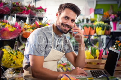 Male florist talking on mobile phone while using laptop