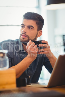 Man drinking coffee while working on laptop