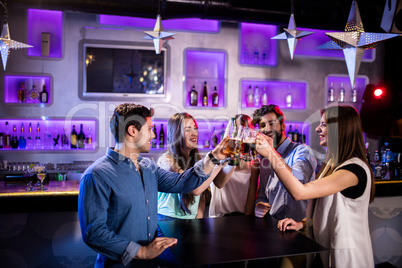 Group of friends toasting beer glasses at bar counter