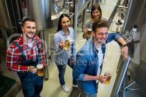 Brewers holding glass of beer standing at brewery