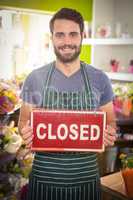 Male florist holding closed signboard at his flower shop