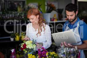 Woman preparing flower bouquet while man using laptop