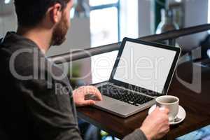 Man holding coffee cup and using laptop