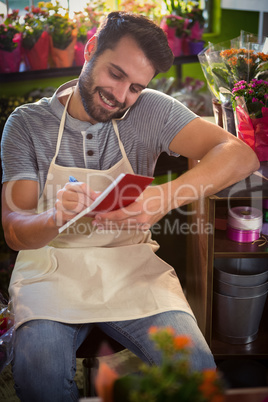 Male florist noting order in dairy while talking on mobile phone