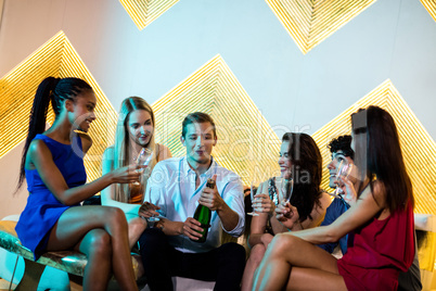 Male friend popping a champagne bottle while friends watching hi