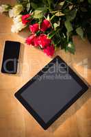 Bunch of roses with smartphone and digital tablet on the wooden