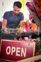 Close-Up of open signboard while of male florist using digital t
