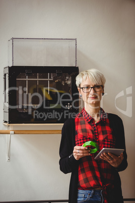 Female graphic designer holding model while using digital tablet