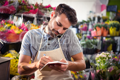 Male florist noting order in diary while talking on mobile phone