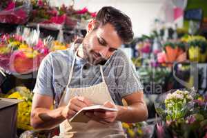 Male florist noting order in diary while talking on mobile phone