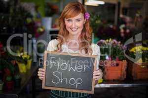 Portrait of female florist holding slate with flower shop sign