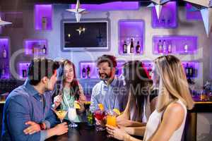 Group of friends interacting with each other at bar counter whil