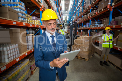 Focus of manager is using a tablet and wearing a hard hat