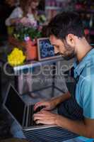 Male florist sitting and using laptop