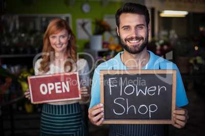 Man holding slate with flower shop sign and woman holding open s