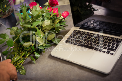 Worktop with laptop and bunch of roses at flower shop
