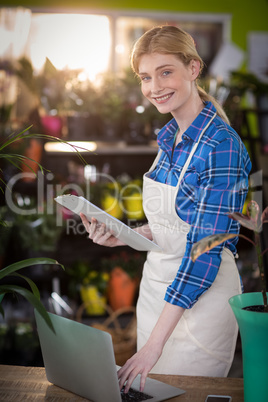 Female florist using laptop while holding clipboard