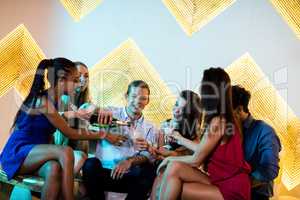 Group of smiling friends sitting on sofa and having a glass of c