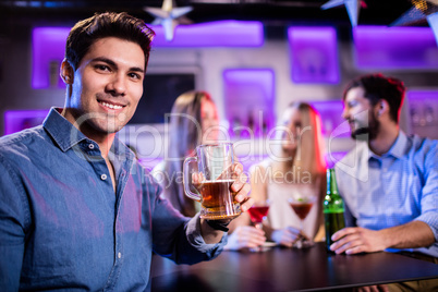 Portrait of young smiling man having glass of beer at bar counte