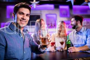 Portrait of young smiling man having glass of beer at bar counte