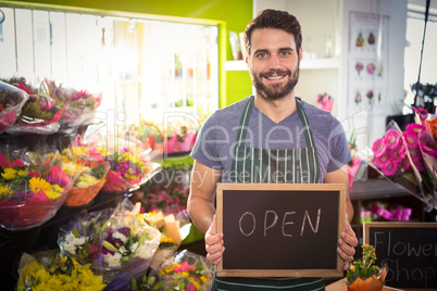 Male florist holding open sign on slate at his flower shop