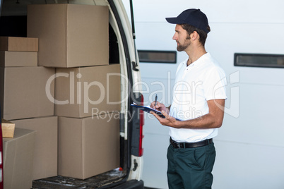 Delivery man is looking his goods and holding a clipboard