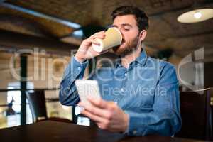 Man having coffee while text messaging on mobile phone