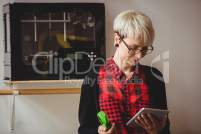 Female graphic designer holding model while using digital tablet