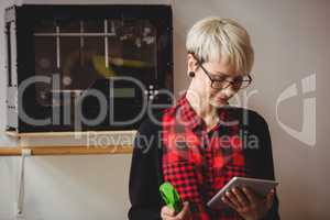 Female graphic designer holding model while using digital tablet
