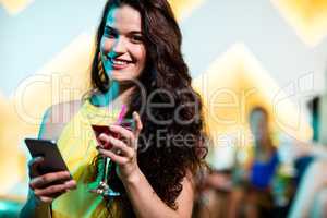 Beautiful woman using mobile phone while having red martini