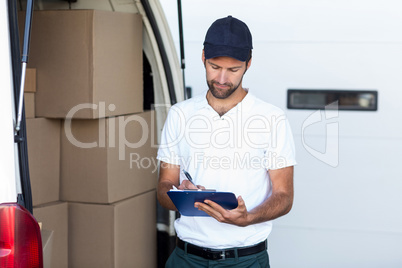 Delivery man is writing on clipboard next to his van