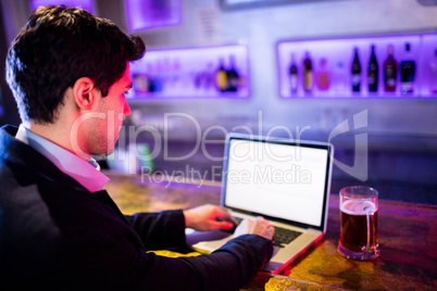 Man using laptop with glass of beer on table at bar counter