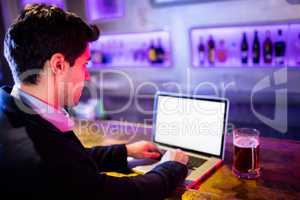 Man using laptop with glass of beer on table at bar counter