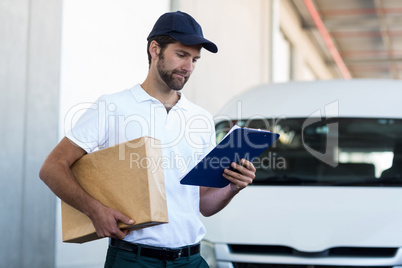 Portrait of delivery man is holding a cardboard box and looking