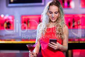 Beautiful woman using mobile phone while having cocktail