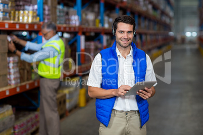 Standing worker smiling at camera while holding digital tablet